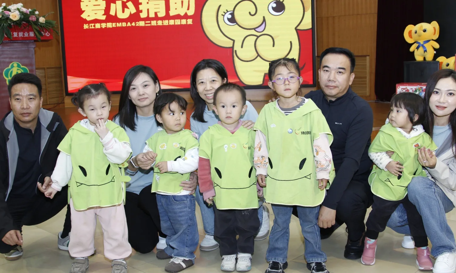 爱心捐助现场合影，背景大屏显示捐助主题
