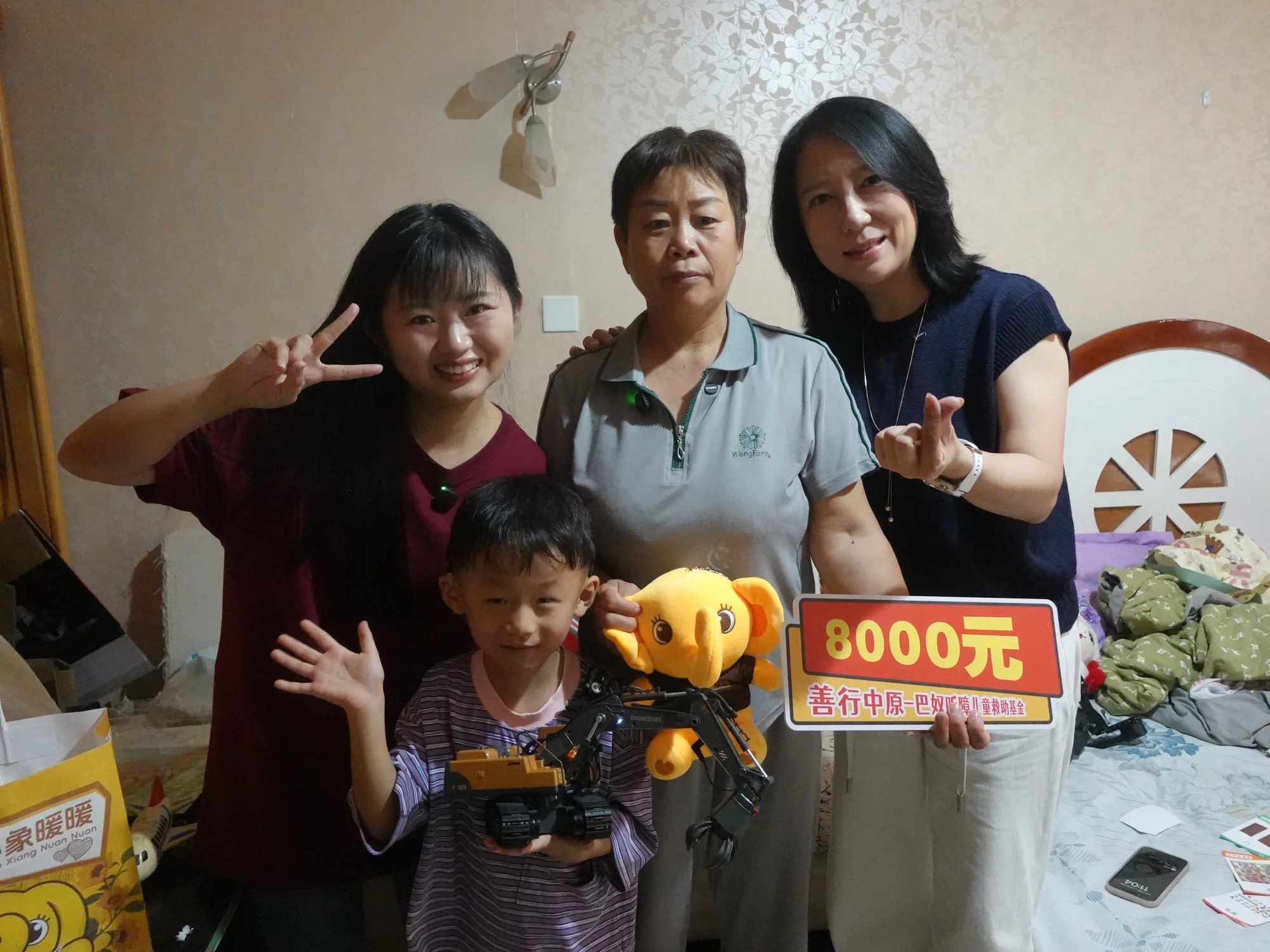 三人与幼儿、小象暖暖公仔合影，手持救助牌