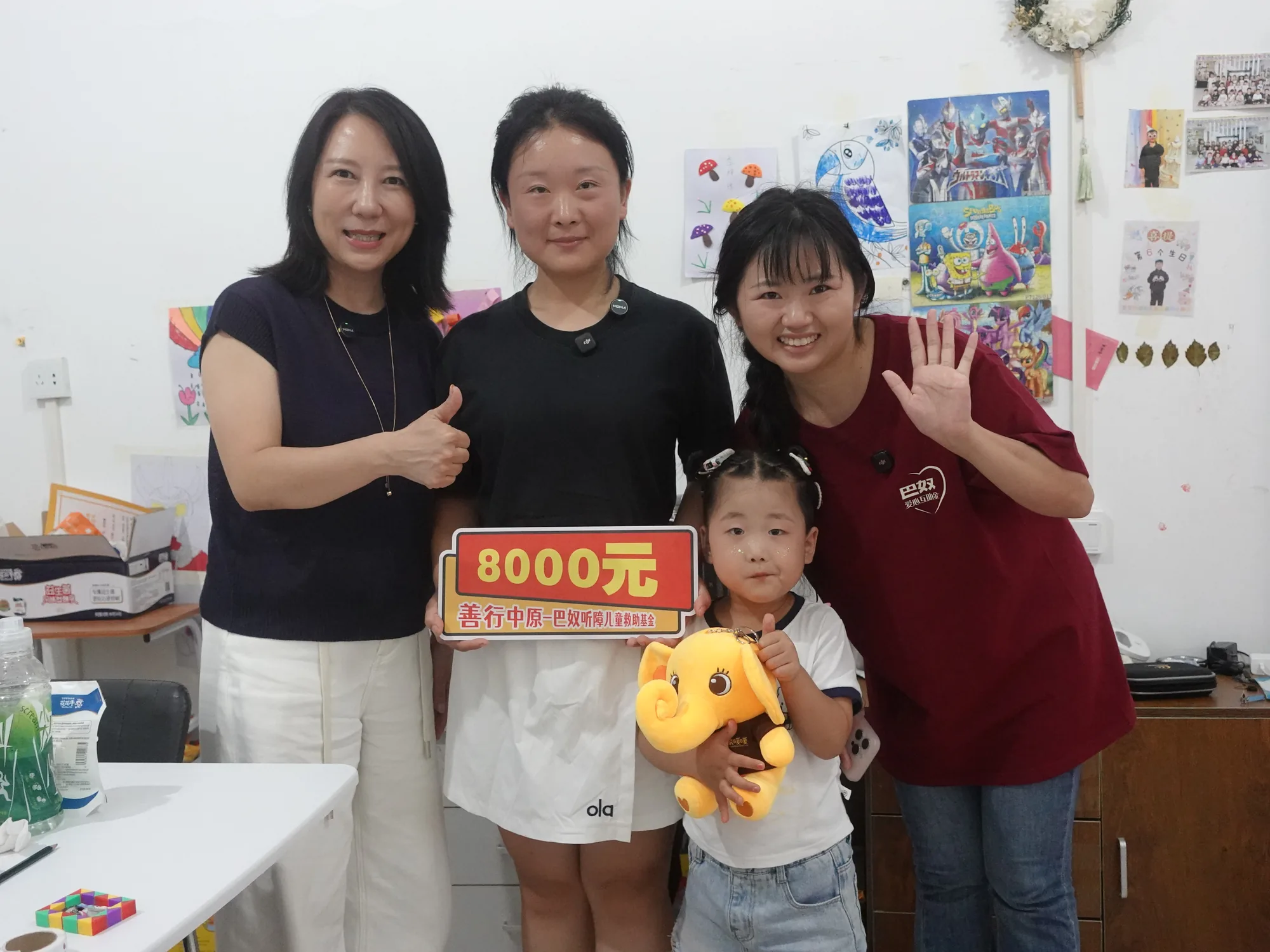 三人与幼儿、小象暖暖公仔合影，手持救助牌