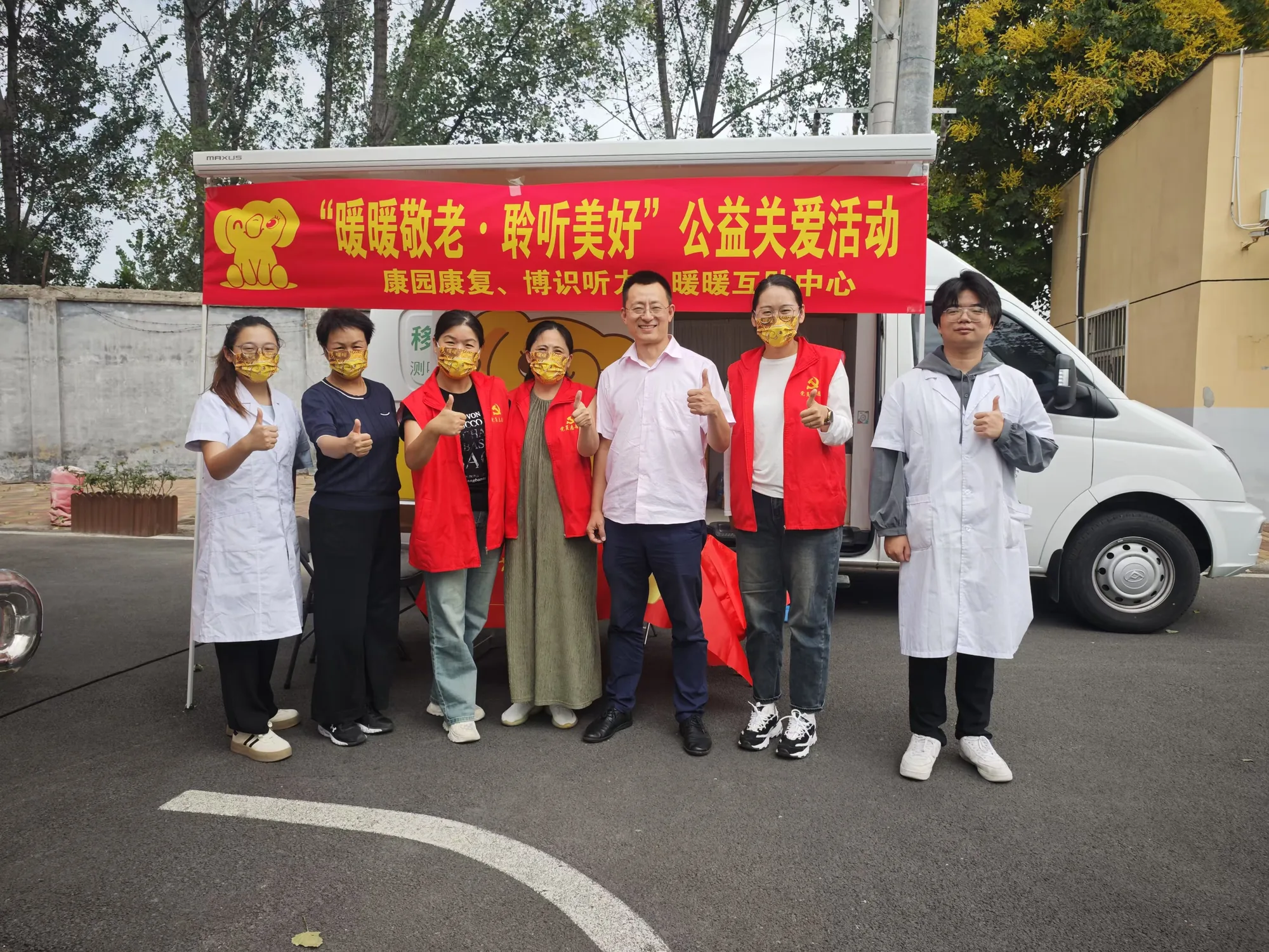 白大褂医生与红马甲志愿者在移动听力服务车前合影